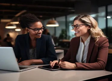 Two professional women discussing precision marketing strategies with digital devices in a modern office.